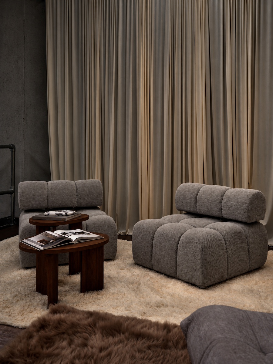 Pair of grey bouclé lounge chairs on a cream rug against floor-length taupe curtains