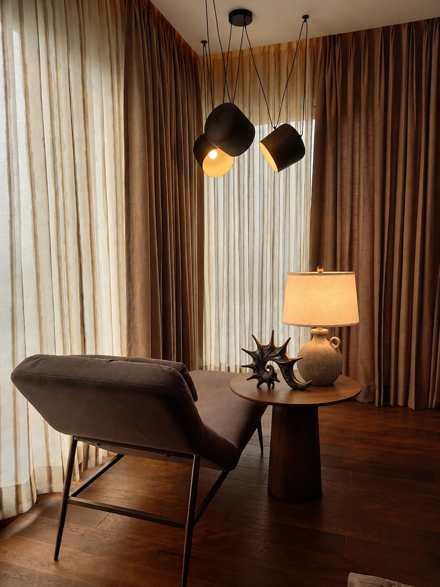 Moody corner with a taupe chaise, round wooden table, lamp and black pendant lights